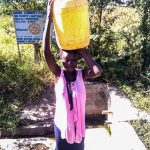 En ung kvinna bär hem vatten från Surudikällan.